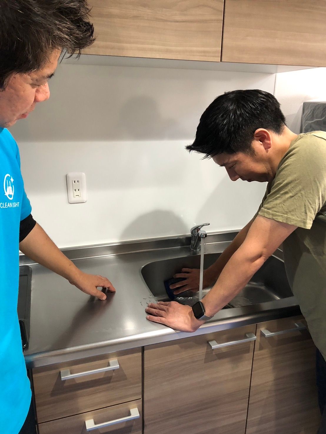 講師が受講生にキッチンの水回り清掃を指導している様子