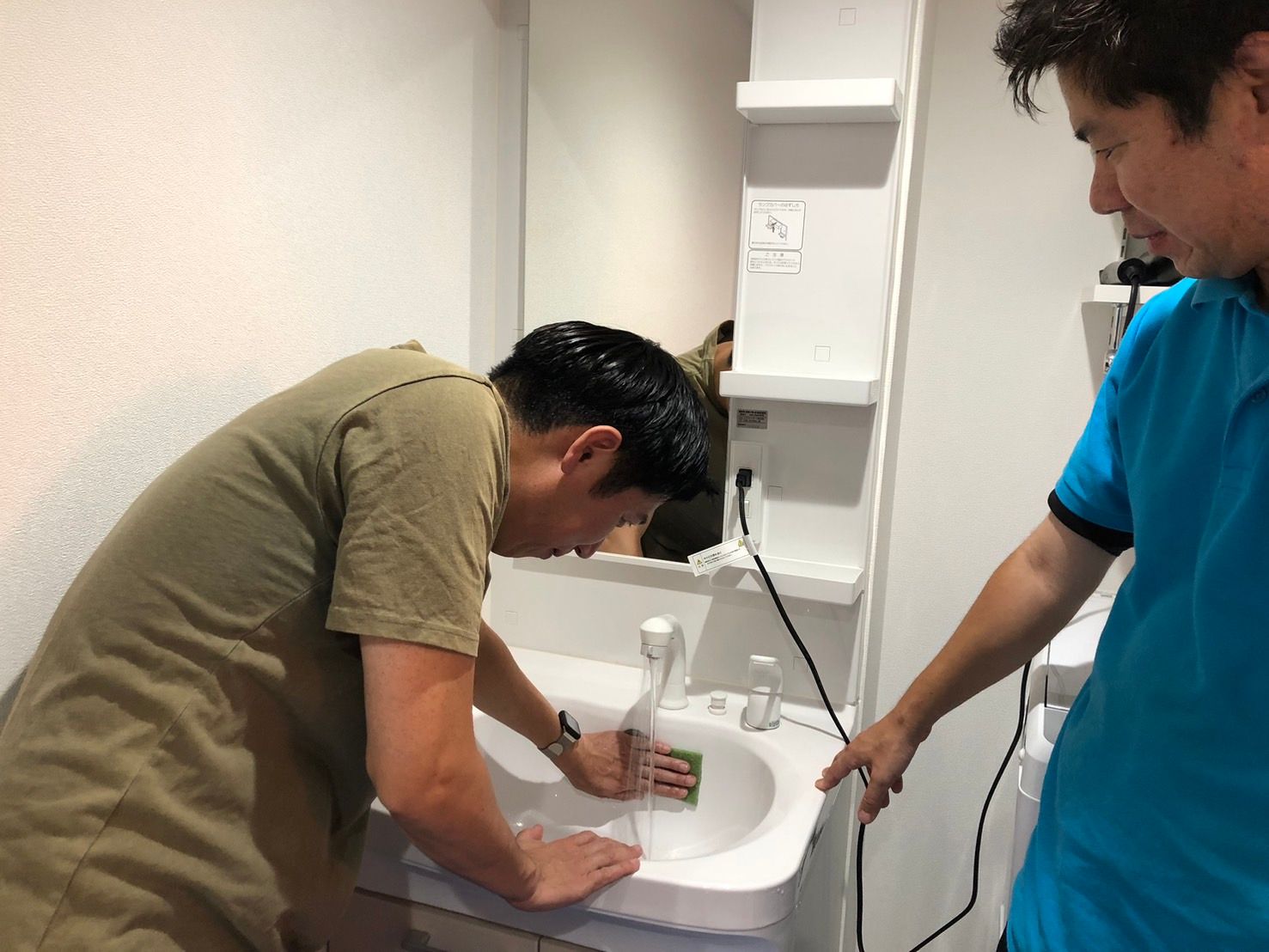 講師が受講生に洗面台の清掃を指導している様子
